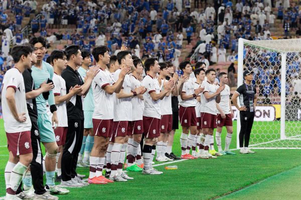 광주 FC 선수들이 AFC 챔피언스리그 경기 종료 후 관중을 향해 박수를 보내며 감사 인사를 전하고 있다. 선수들은 흰색 유니폼 상의와 자주색 하의 차림이며, 배경에는 푸른 유니폼을 입은 알힐랄 팬들이 경기장을 가득 메우고 있다.