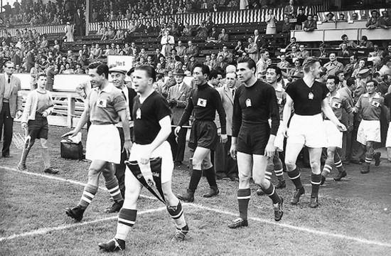 1954년 스위스 월드컵에서 헝가리와 대한민국 축구 대표팀 선수들이 경기장에 입장하고 있는 모습. 헝가리 선수들은 어두운색 유니폼, 대한민국 선수들은 밝은 상의와 태극기 마크가 달린 유니폼을 착용하고 있으며, 배경에는 관중석이 가득 차 있다.
