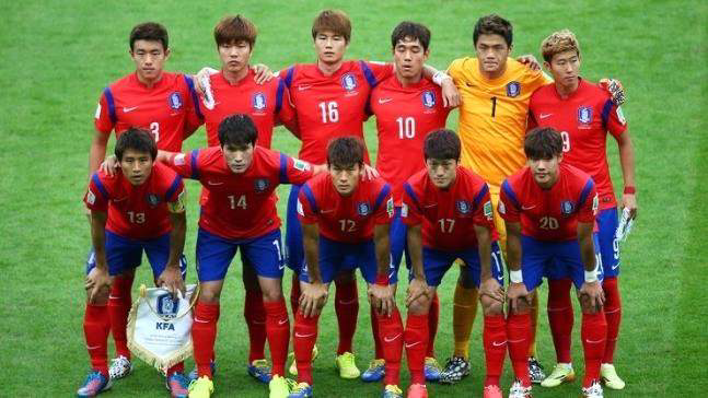 2014 브라질 월드컵 경기 전, 대한민국 축구 국가대표팀 선수들이 붉은색 유니폼을 입고 단체 사진을 촬영한 모습. 선수들이 앞줄과 뒷줄로 나뉘어 서 있으며, 배경은 경기장 잔디.