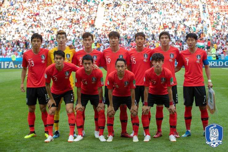 2018 러시아 월드컵 조별리그 경기 전, 대한민국 축구 국가대표팀이 붉은색 유니폼을 입고 경기장에 나서기 전 단체 사진을 촬영하는 모습. 앞줄과 뒷줄로 나뉘어 11명의 선발 선수가 포즈를 취하고 있으며, 오른쪽 끝에는 주장 완장을 찬 손흥민이 서 있다. 경기장에는 많은 관중이 관람 중이다.