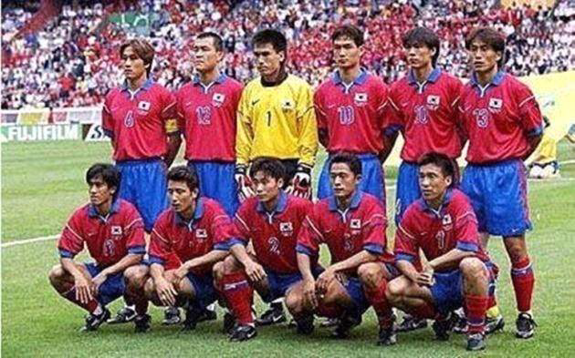 1998년 프랑스 월드컵 경기 전에 촬영된 대한민국 축구 국가대표팀의 단체 사진. 붉은색 상의와 파란색 하의를 착용한 선수 11명이 두 줄로 나뉘어 포즈를 취하고 있으며, 가운데에는 노란색 골키퍼 유니폼을 입은 김병지가 있다. 뒤편 관중석은 가득 찬 응원단으로 붉은 물결을 이루고 있으며, 배경에는 FIFA와 후지필름 광고판이 보인다.